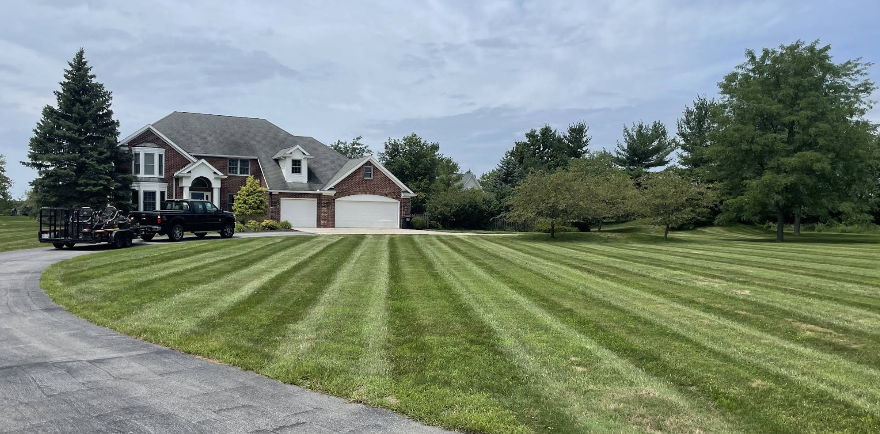Freshly striped lawn mowed by Affordable Lawn Care Company with truck and trailer in driveway, Lima Ohio